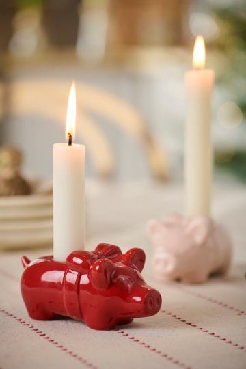 Röd julgris och rosa julgris som ljusstakar med tänt ljus på juldukat bord