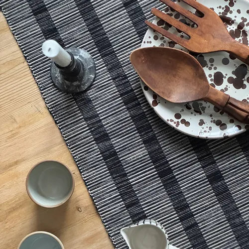 Randig bordslöpare i svart och linnefärgad återvunnen textil på träbord med rustik dukning