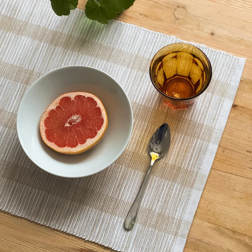Randig bordstablett i vitt och grått med skål grapefrukt glas och sked på träbord