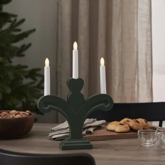 Grön adventsljusstake Orsa med tre tända LED-ljus placerad på ett träbord i en ombonad julmiljö.