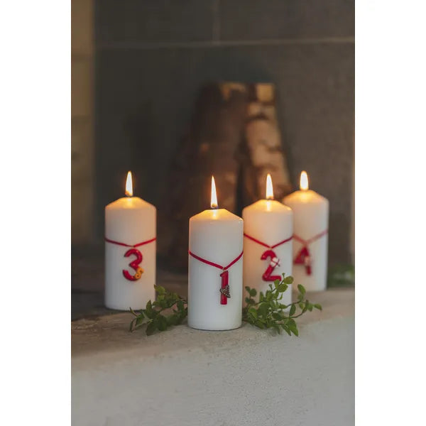 Röda adventssiffror 1–4 från Nääsgränsgården fastsatta på blockljus som står uppställda vid en öppen spis