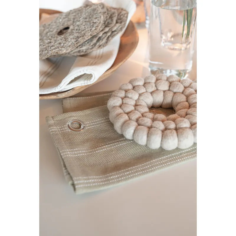 Runt grytunderlägg RULLE i beige ull med tät struktur av små bollar på dukat bord
