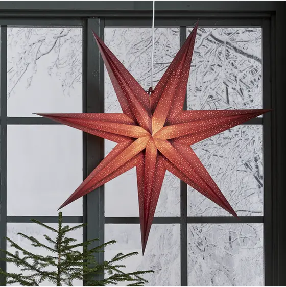 Röd adventsstjärna Holly med varmt ljussken upphängd i ett fönster som stämningsfull juldekoration.