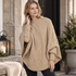 Modell i beige stickad poncho Nora med kabelstickning