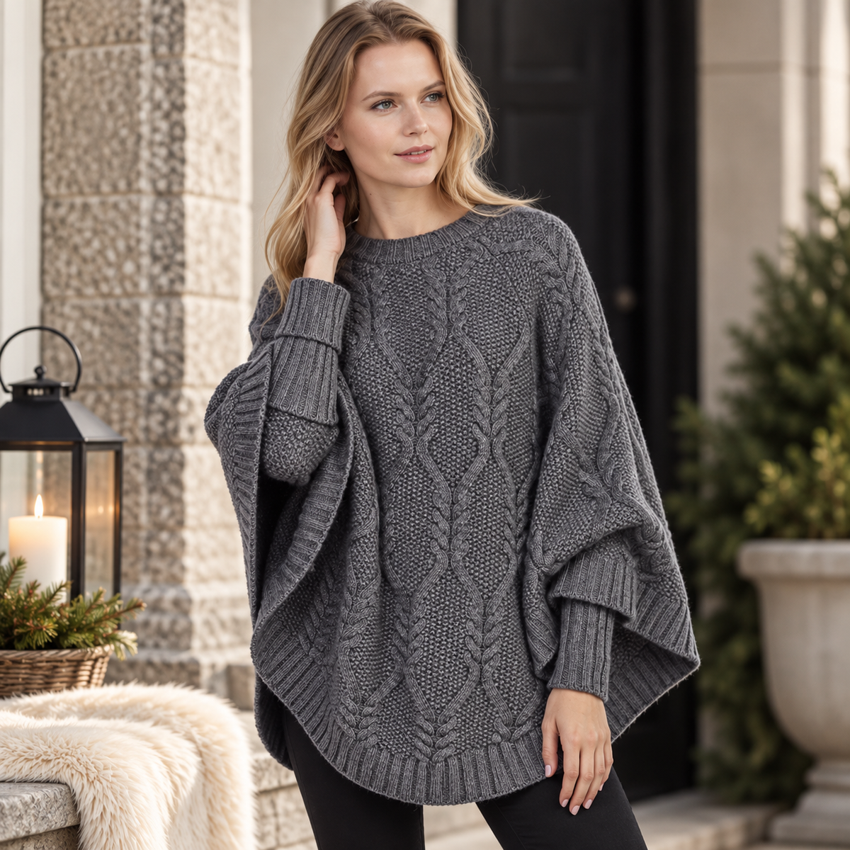 Modell i mörkgrå stickad poncho Nora med kabelstickning
